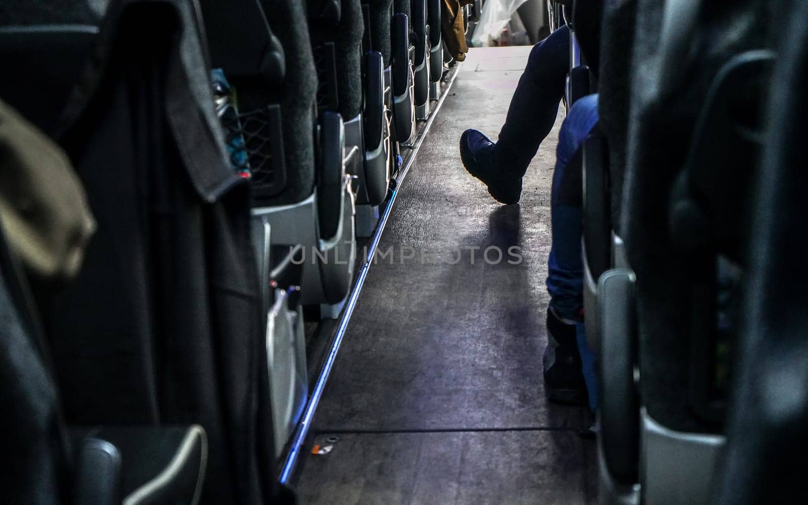 Coach bus seats seen from back row, one passenger has his foot in aisle. by Ivanko