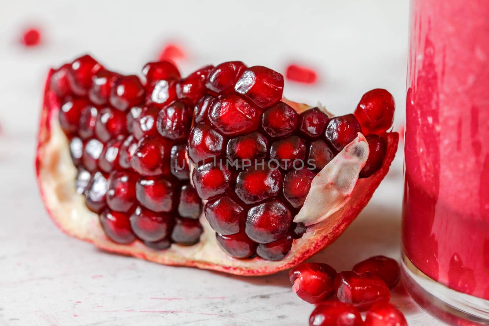 Detail photo - portion of pomegranate, cluster of gem like fruits visible, glass with pink smoothie on the right