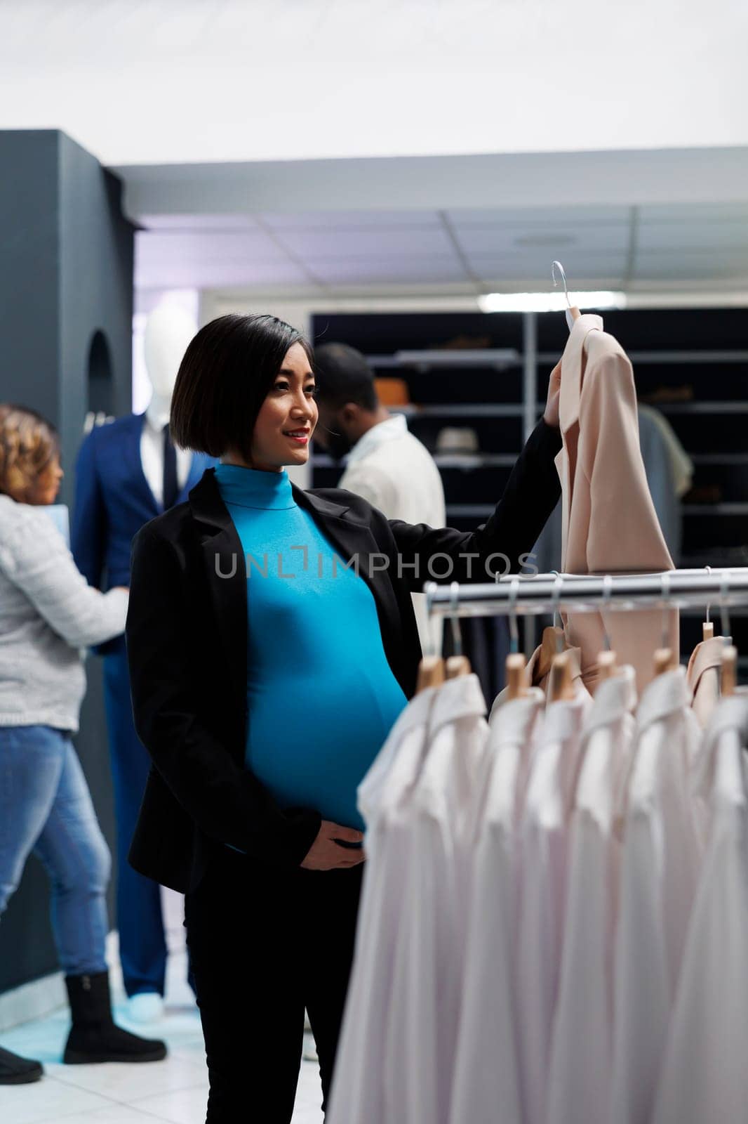 Pregnant woman examining jacket in mall by DCStudio