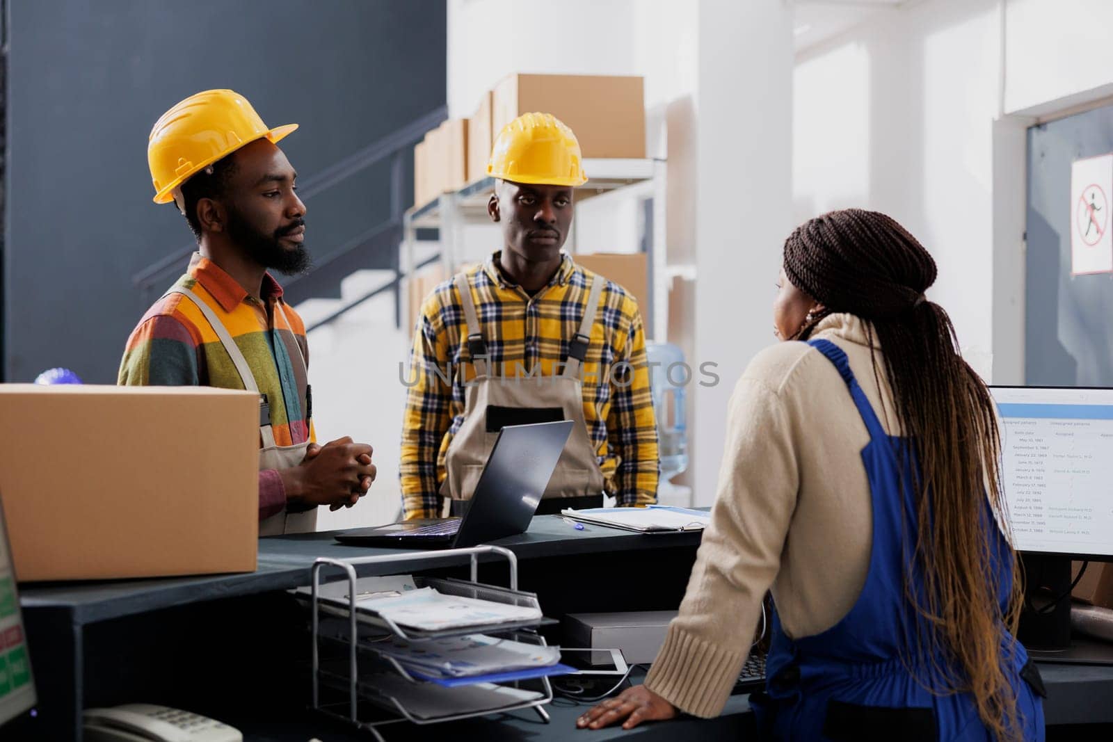 Storehouse employees discussing pacel delivery delay with shipment manager at post office counter desk. All black warehouse coworkers team talking about packages dispatching