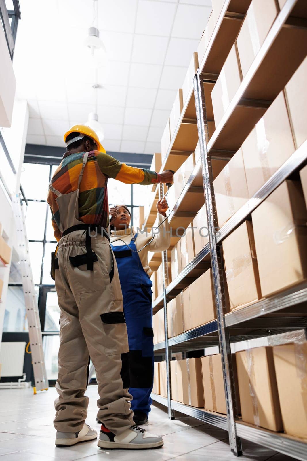 African american warehouse worker scanning parcel for logistics manager. Distribution operator pointing at cardboard box on shelf and storehouse assitant using barcode scanner tool