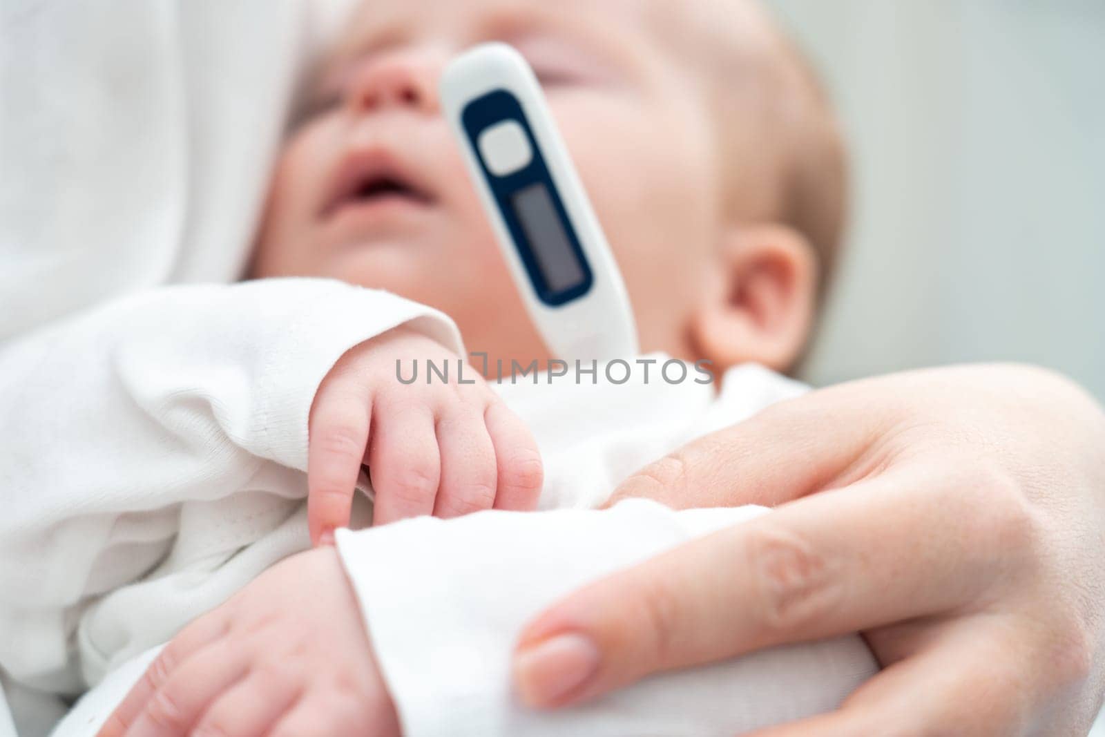 Newborn in deep sleep held by mother as she uses a modern thermometer to detect potential sickness