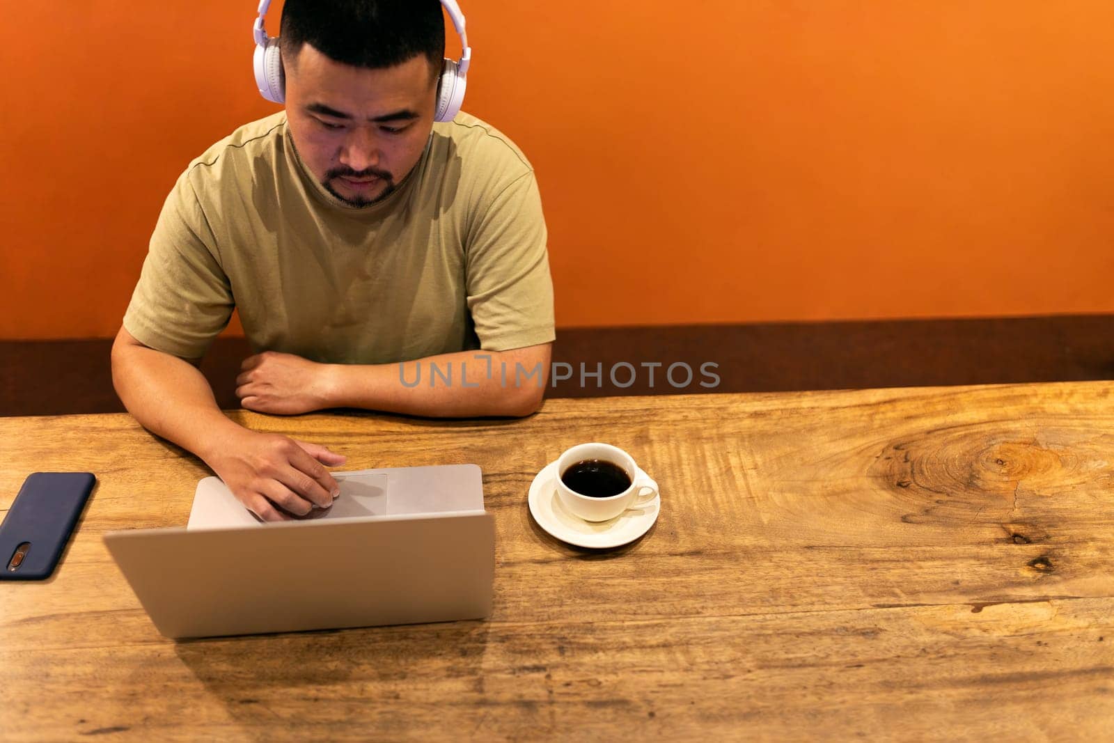 High angle view of Asian male freelance worker with headphones using laptop working in coffee shop. Copy space. Banner. Digital nomad concept.