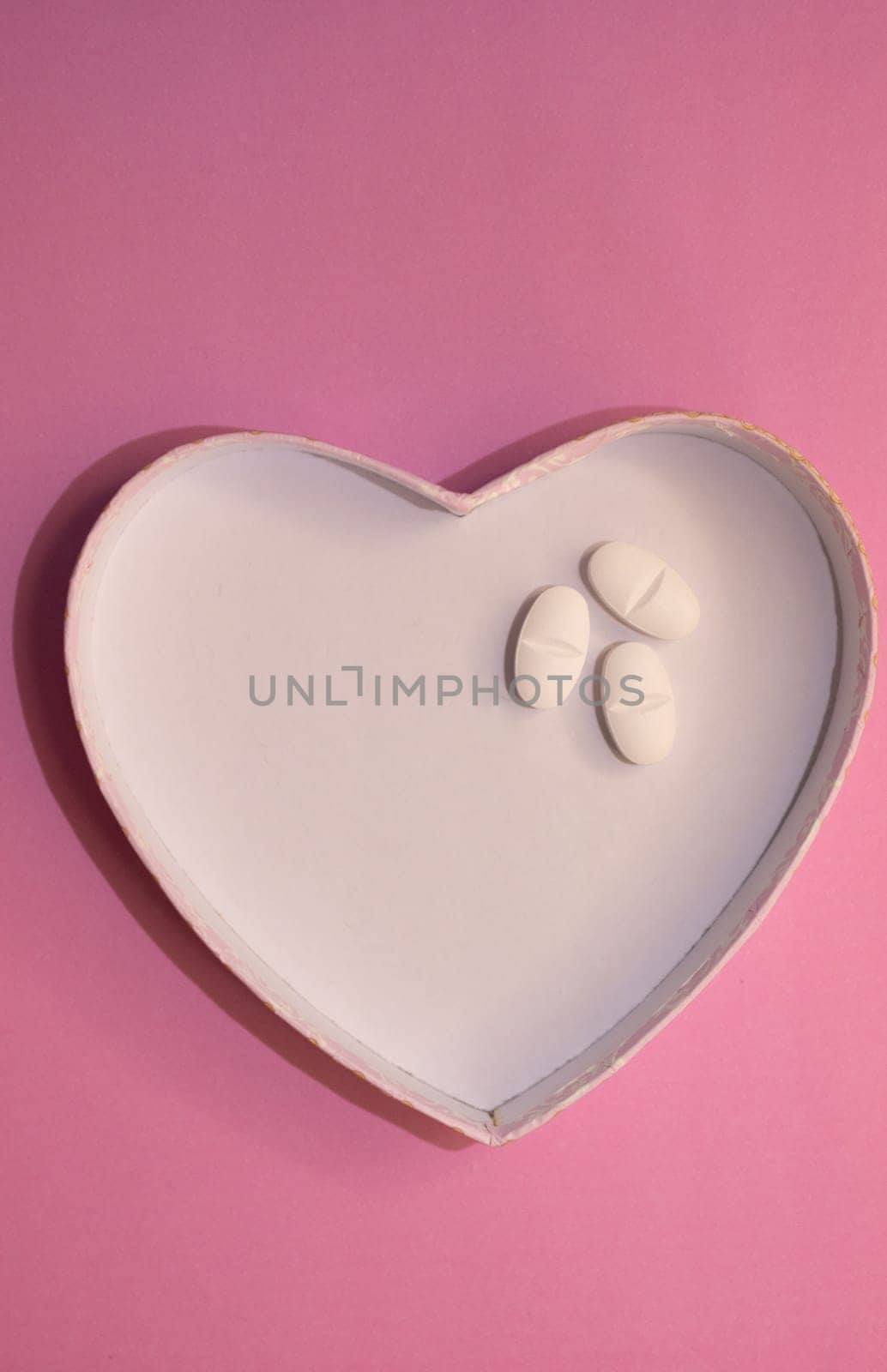 Vertical shot of heart-shaped figure with pills on pink background. by VeroDibe