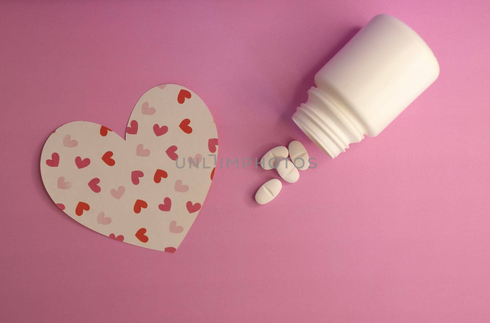 Heart-shaped figure with white capsule bottle on pink background. by VeroDibe