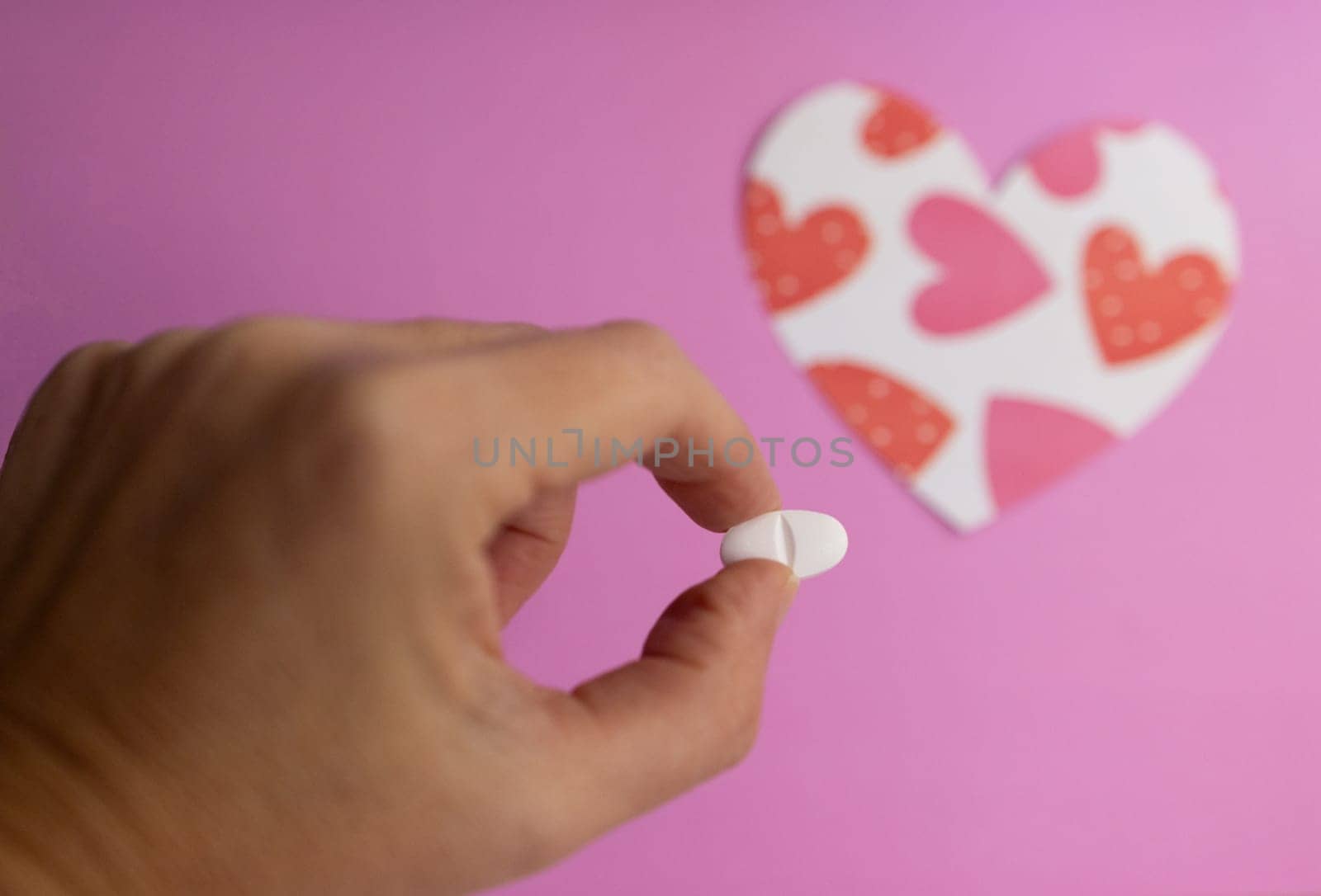 Close-up of fingers holding a pill. Background with blurred heart figure by VeroDibe