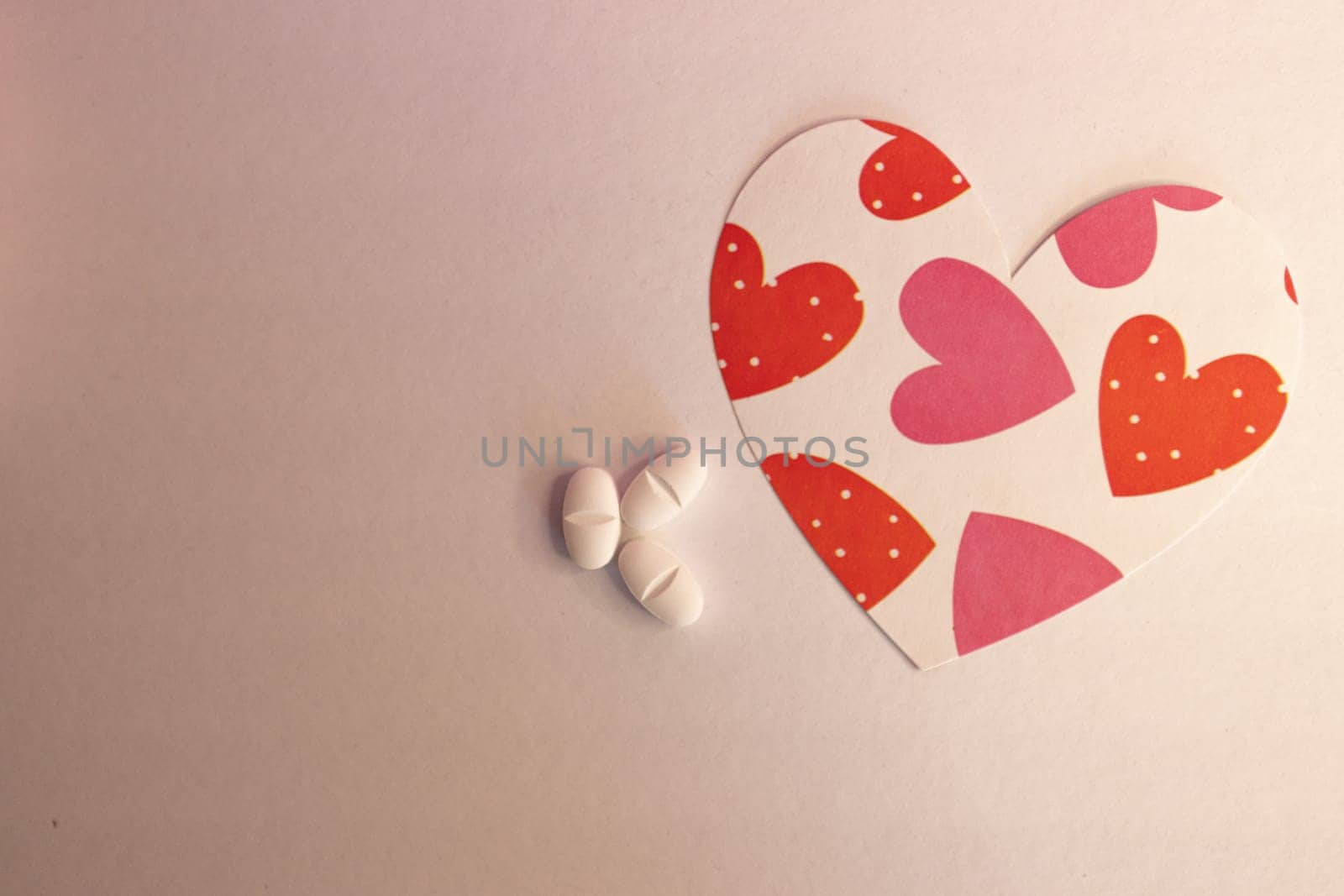 Heart-shaped figure with print with white capsules in light background. by VeroDibe