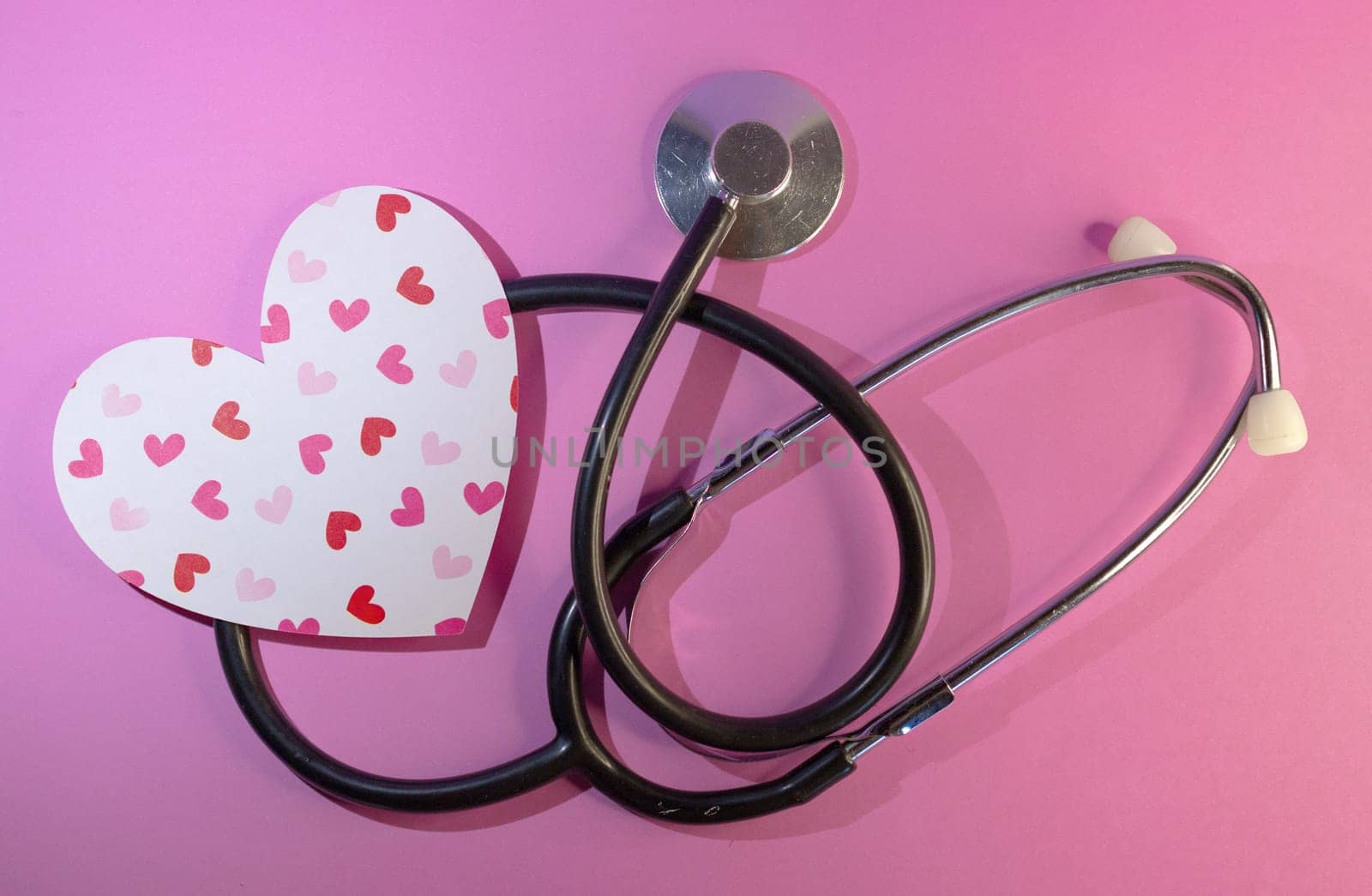 Stethoscope with an image of heart printed on pink background. by VeroDibe