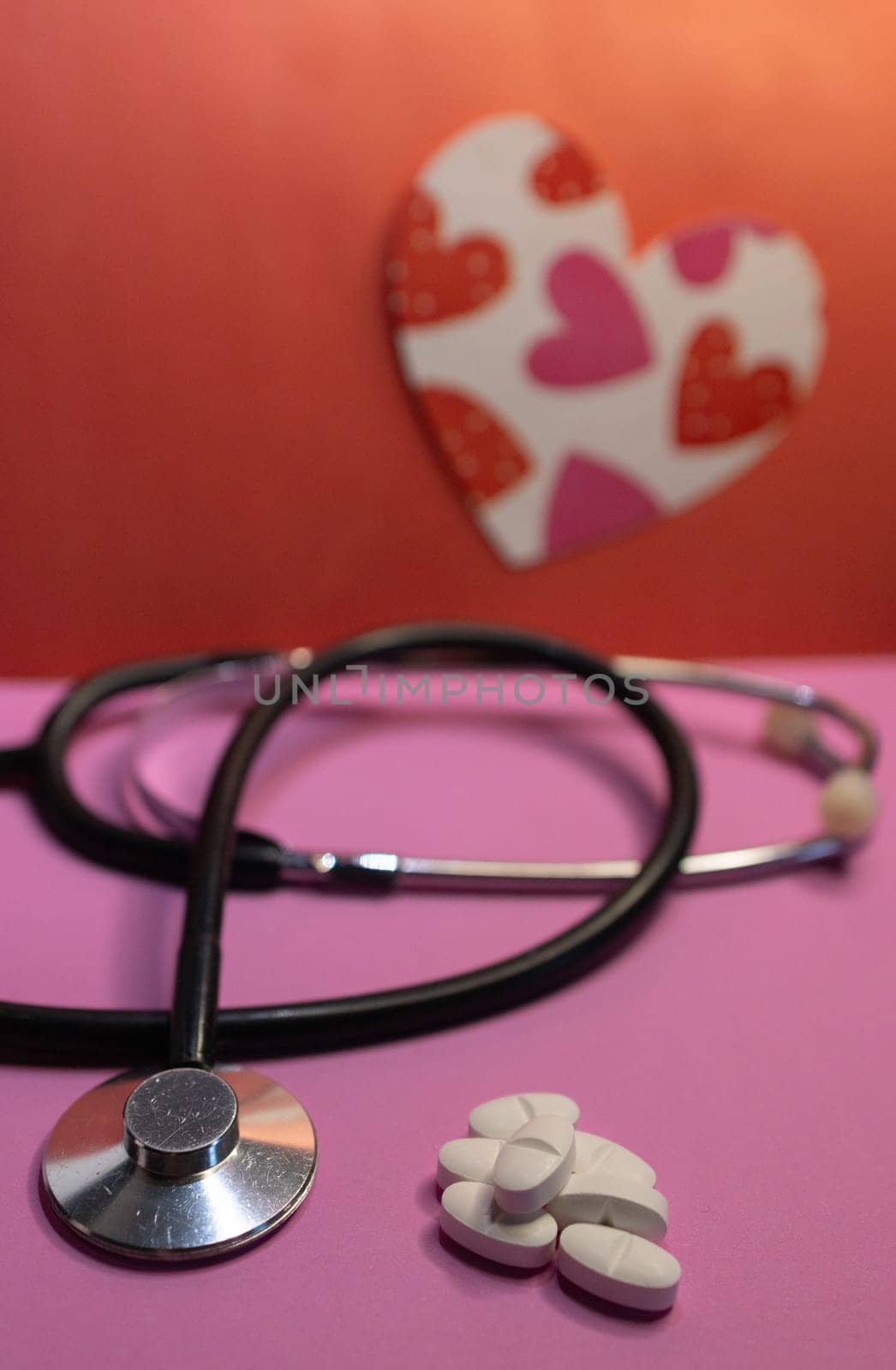 Stethoscope with pills in the foreground, heart image on blurred background. by VeroDibe