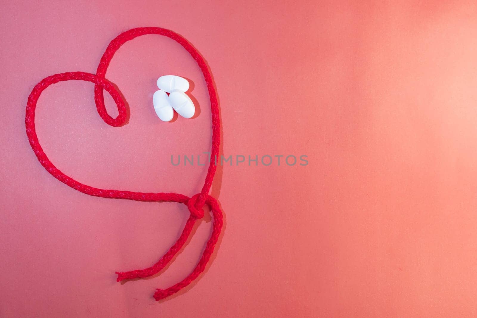 Horizontal top view of red string in the shape of a heart with white tablets by VeroDibe