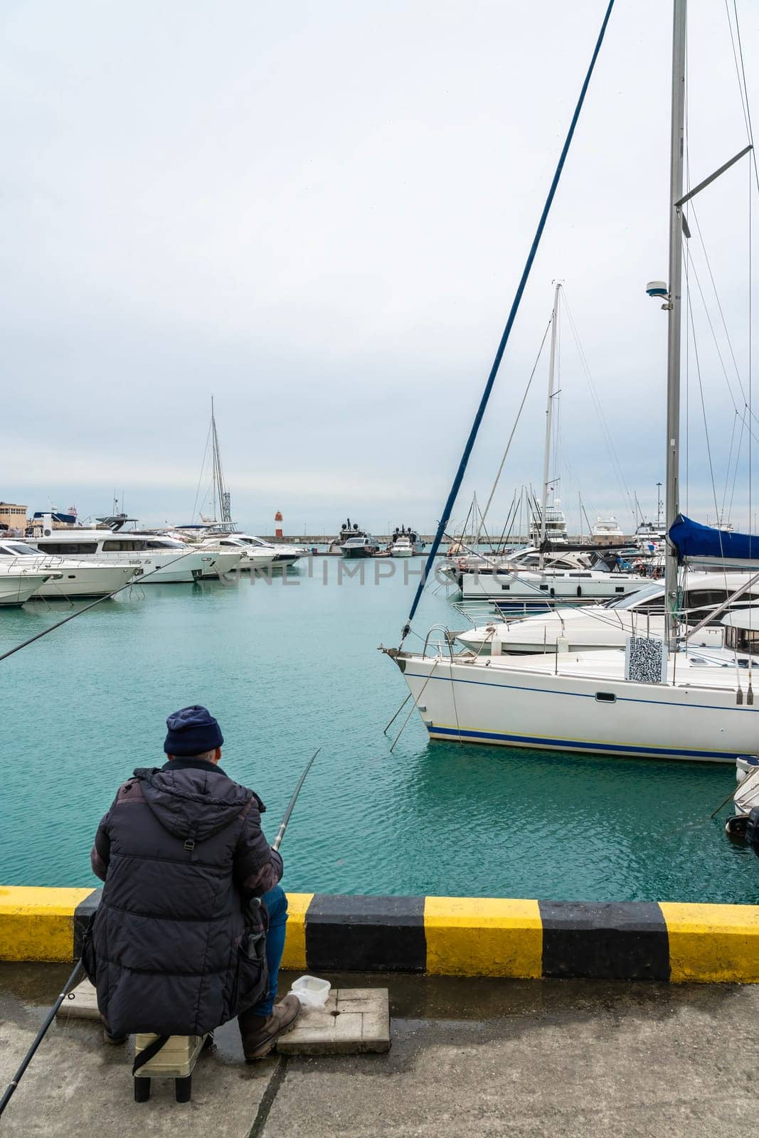 a fisherman catches fish on the background of yachts by roman112007