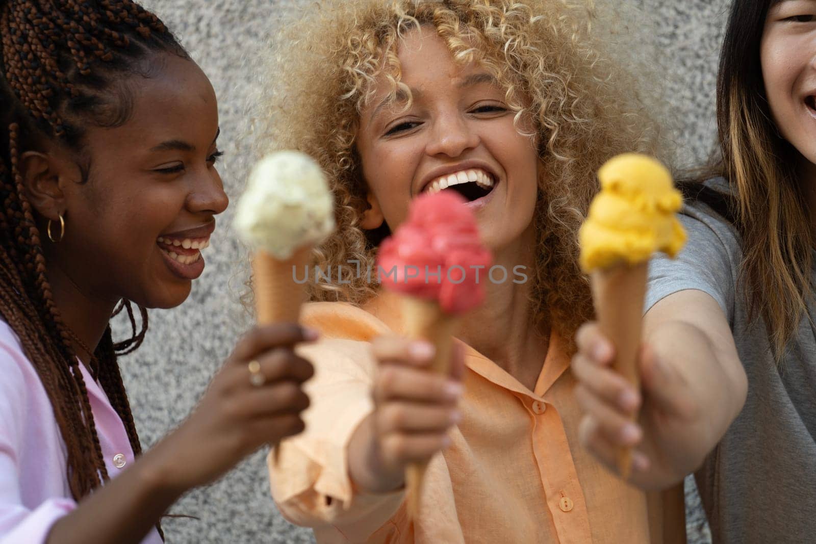 Three happy multiethnic friends welcome summer holding an icecream.