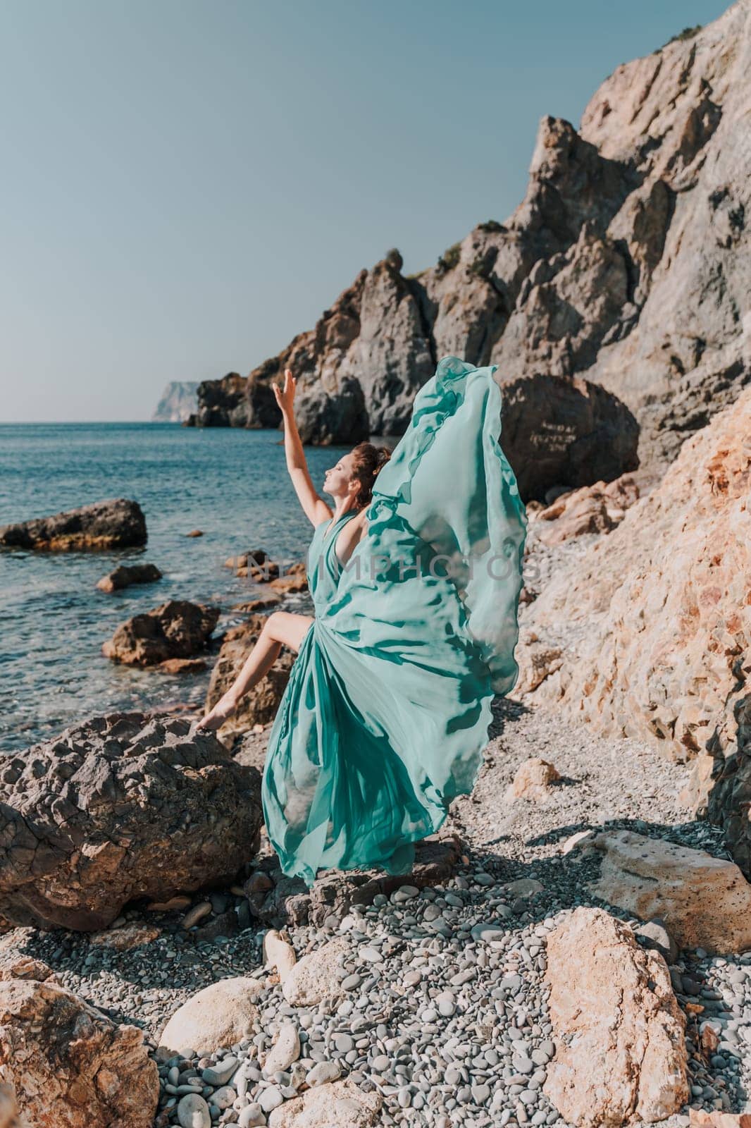 Woman green dress sea. Woman in a long mint dress posing on a beach with rocks on sunny day. Girl on the nature on blue sky background