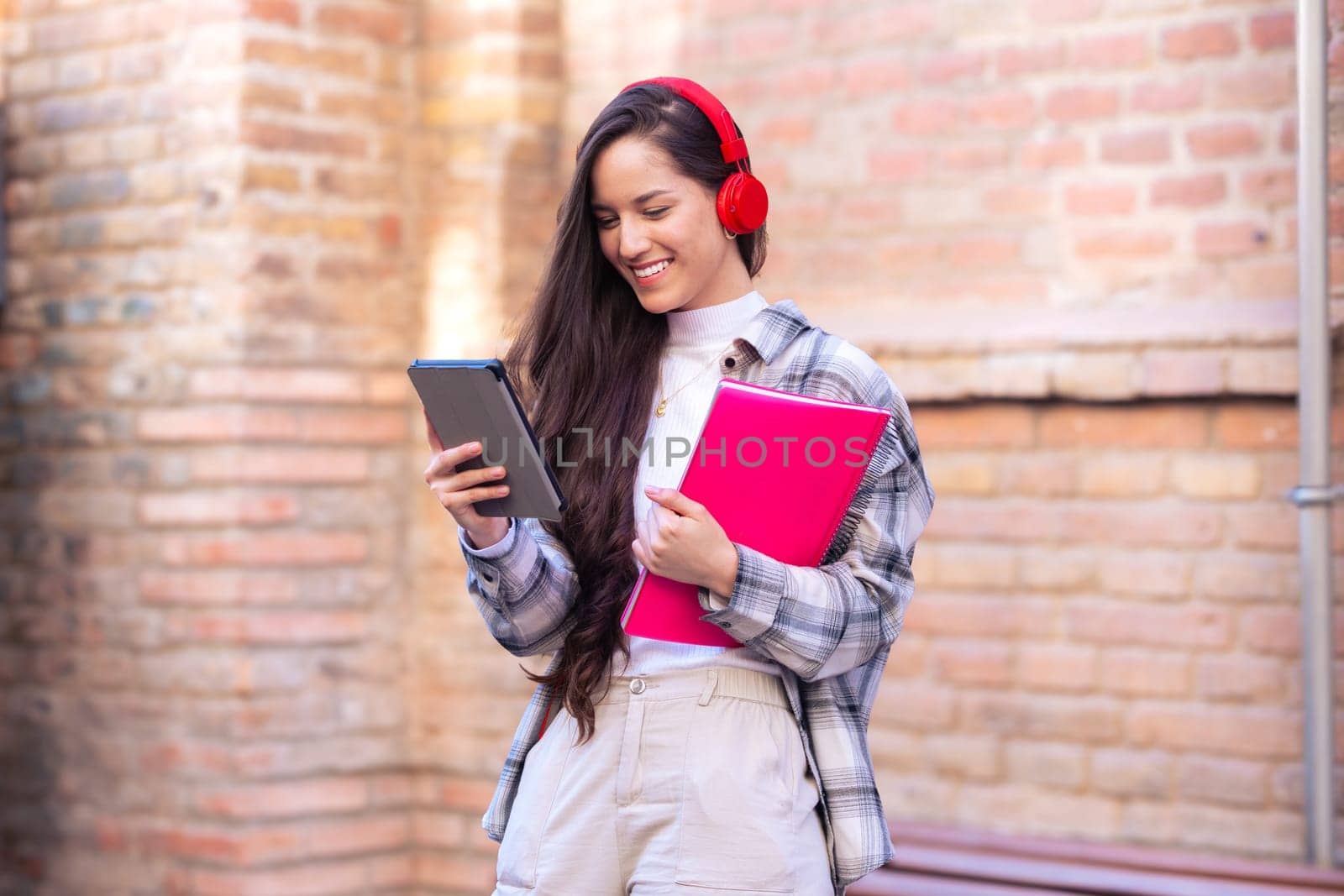 Young smiling student with notebook in hand uses social networks with tablet applications and wireless technology outdoors.