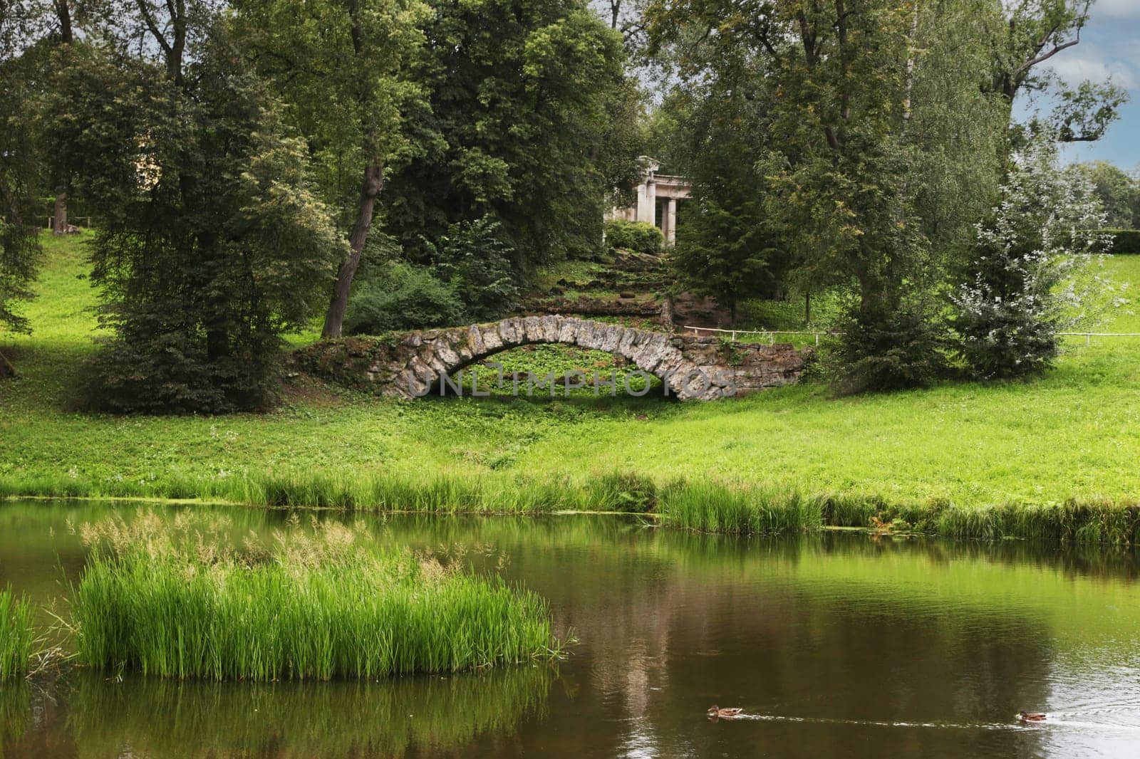 Stone bridge, pond in a recreation park in good weather.