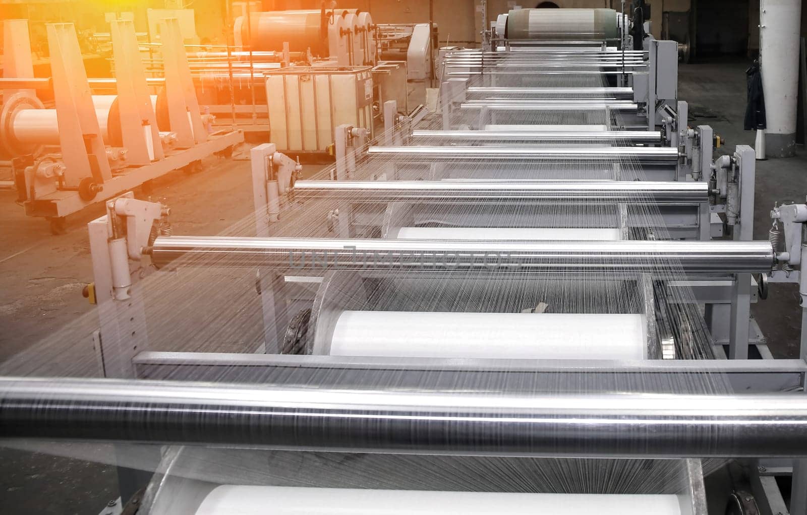 Factory with advanced machines producing white synthetic fibers. Continuous process with large spools in a high-ceilinged building, showcasing efficient manufacturing.