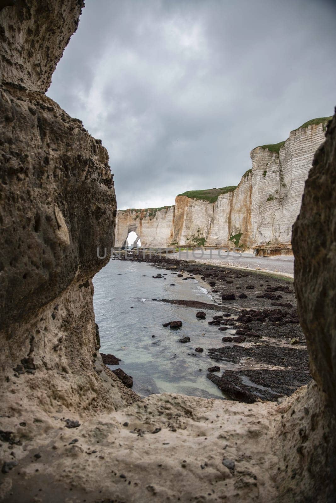 Landscape photo of tall, steep limestone cliffs by the ocean with one with a hole in it creating an arch view from the beach