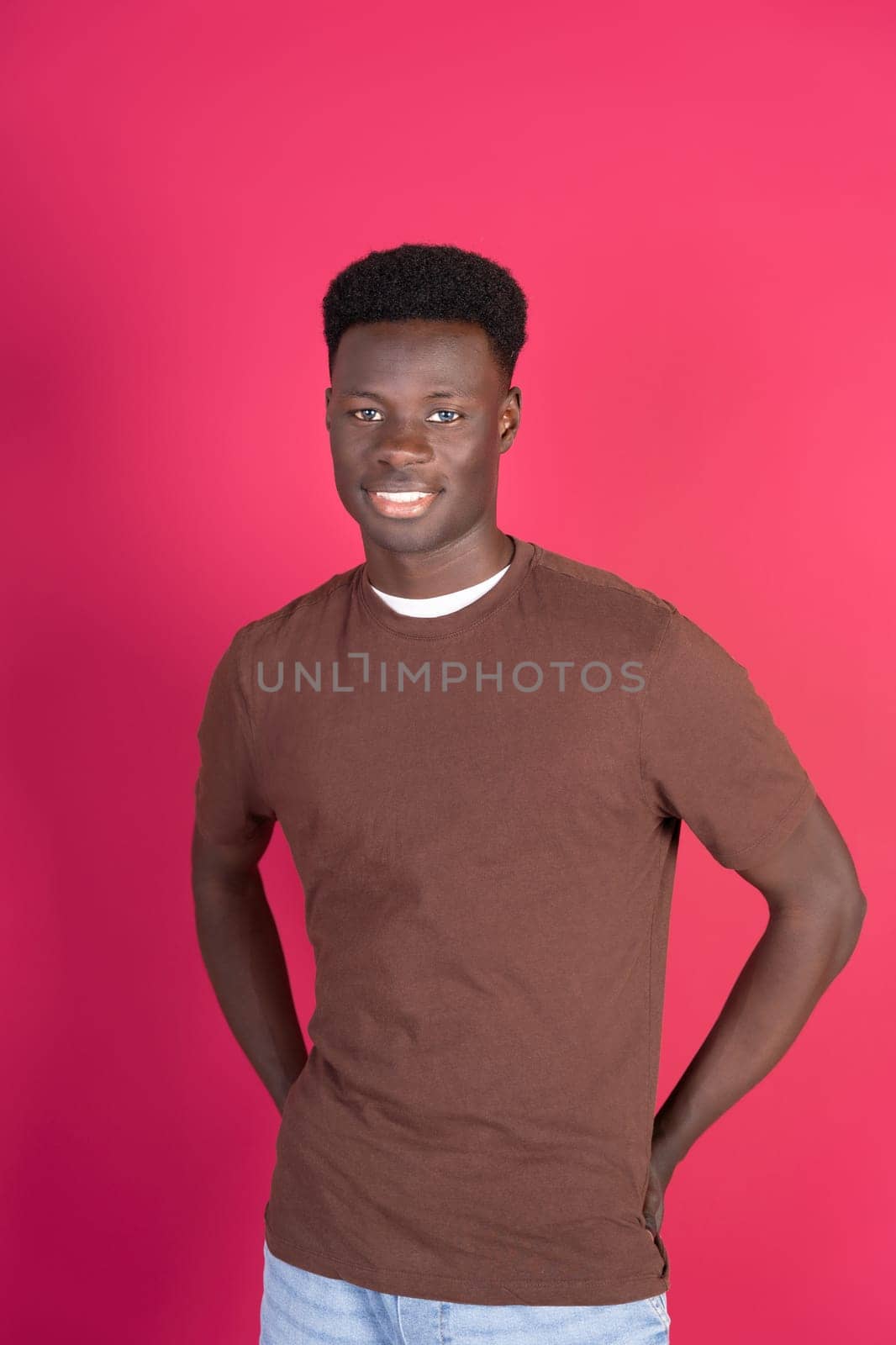 A man with a brown shirt and black hair is smiling for the camera. The image has a warm and friendly mood, with the man's smile and the bright pink background