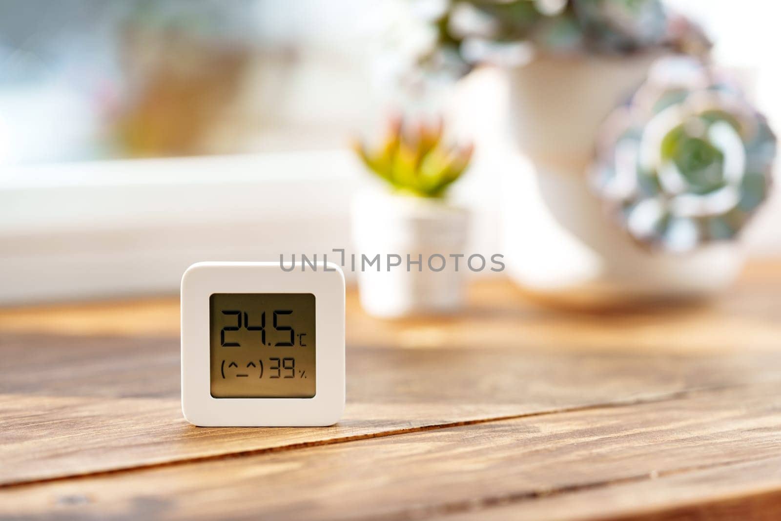 This image shows a digital thermometer sitting on a wooden table in front of a window.