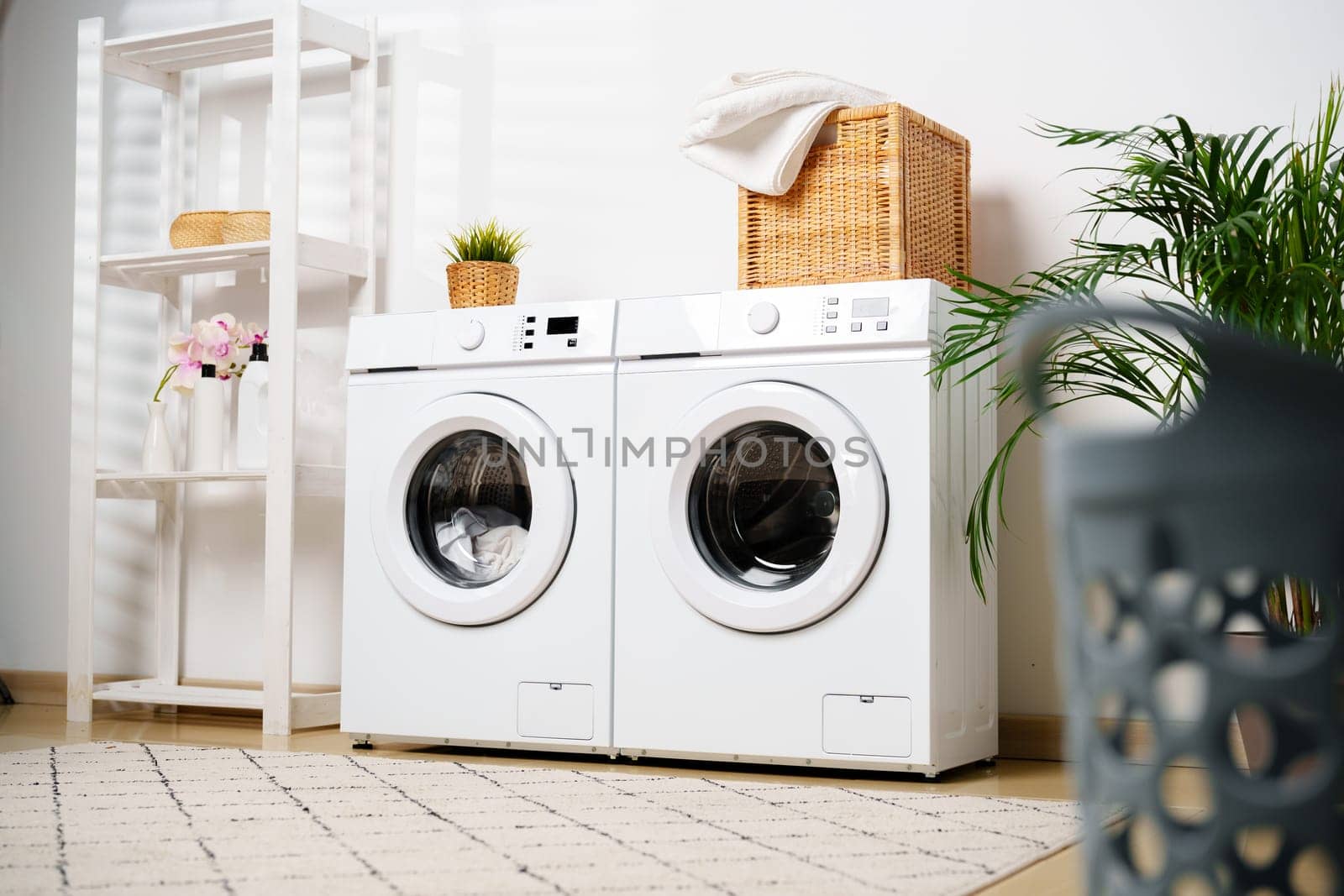 A pile of clean, colorful laundry sits on the floor in front of two white washing machines in a modern laundry room.