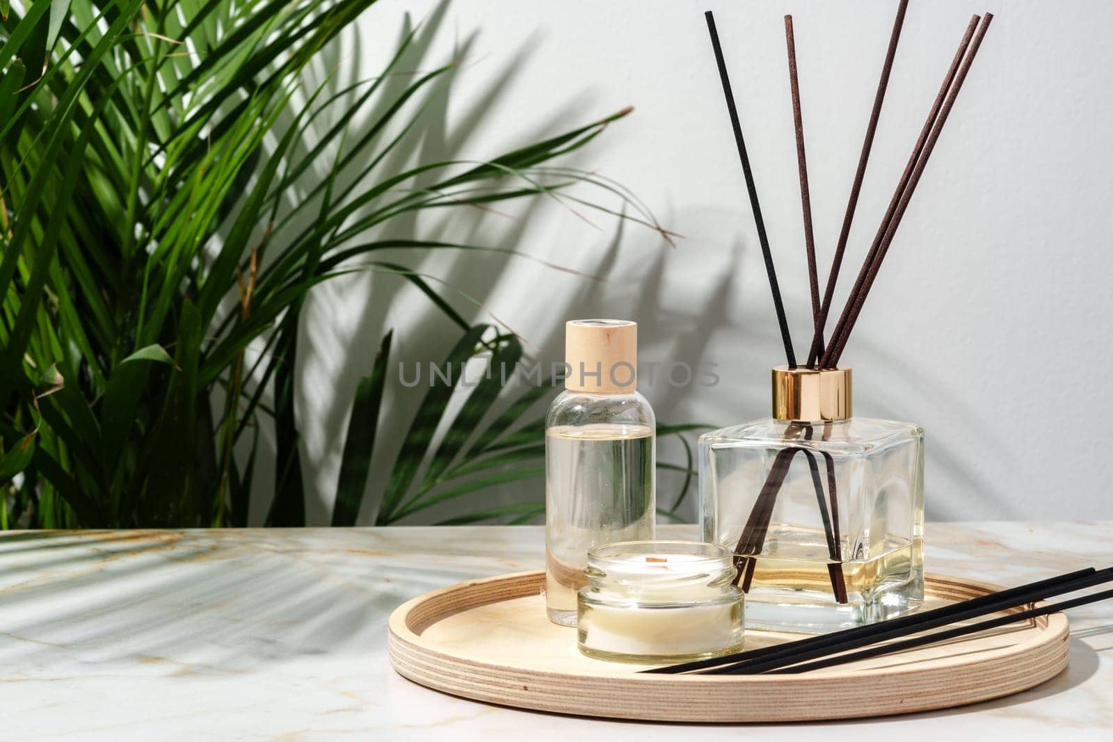 A black reed diffuser, an amber candle, and a wooden tray sit on a white surface.