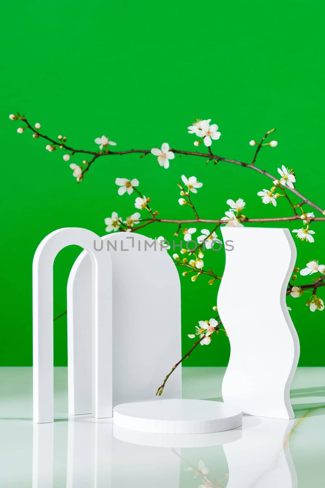 Decorative podiums and blooming branches on green background with shadows copy space