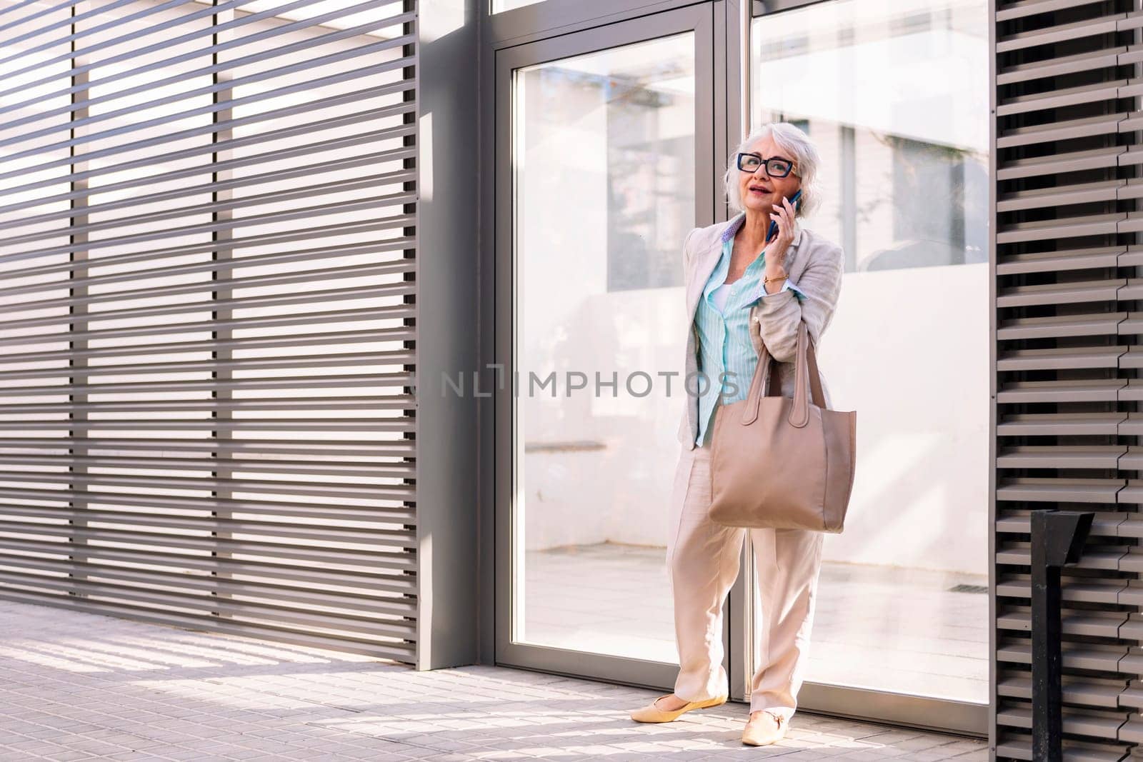 smiling mature woman coming out of the home portal while talking on mobile phone, concept of happiness and technology of communication, copyspace for text