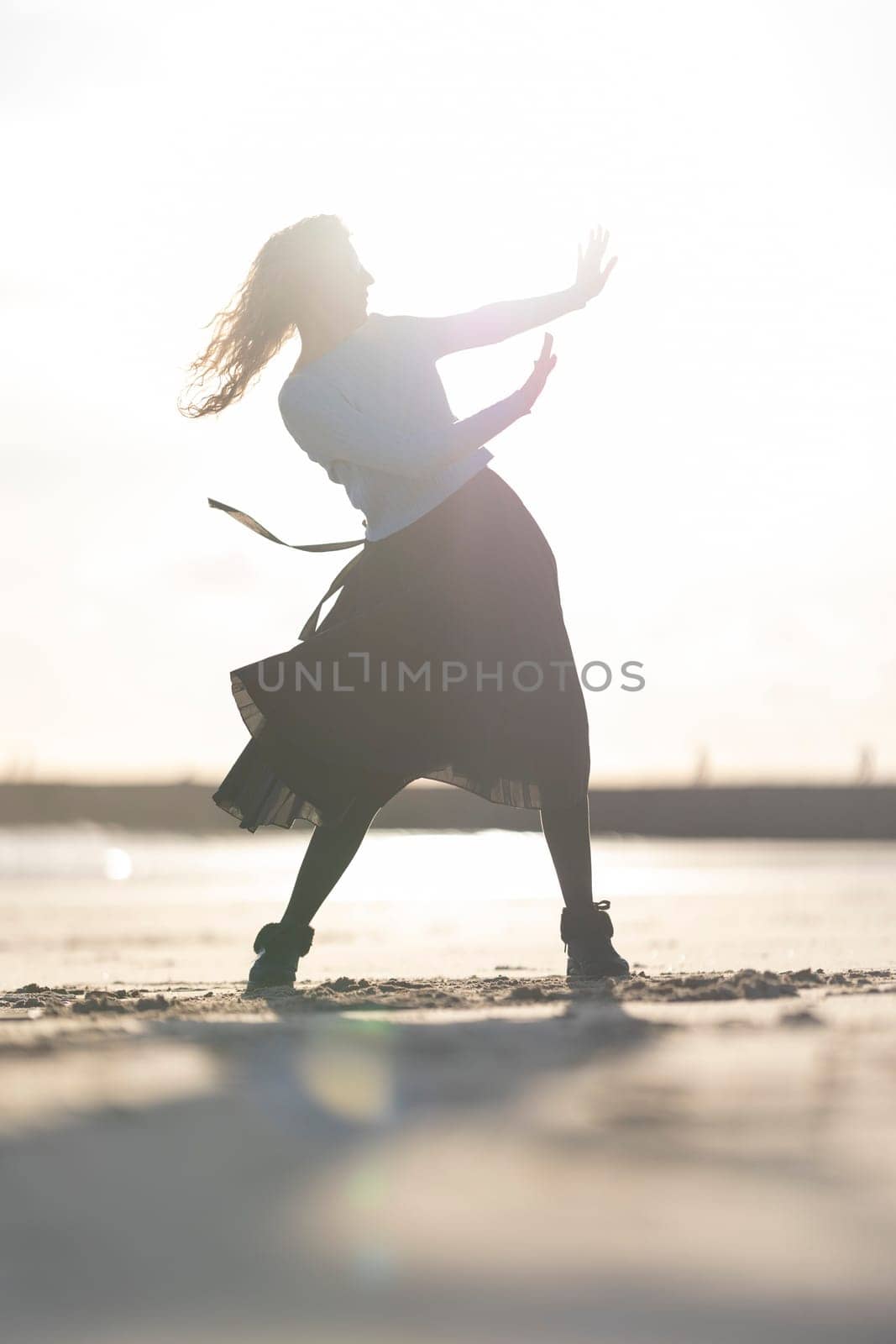 A woman is dancing on the beach in a skirt. Concept of freedom and joy, as the woman is fully engaged in her dance and he is enjoying herself. The beach setting adds to the overall mood of relaxation