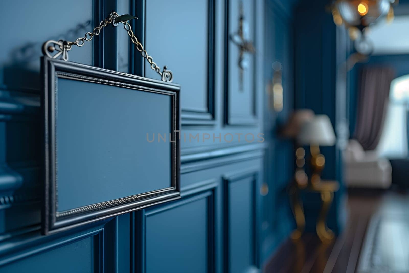 A close-up image of a black framed sign hanging on a blue wall with decorative molding. The sign is blank and has a chain attached to it. The sign is hanging on the left side of the image, and the background is blurred.