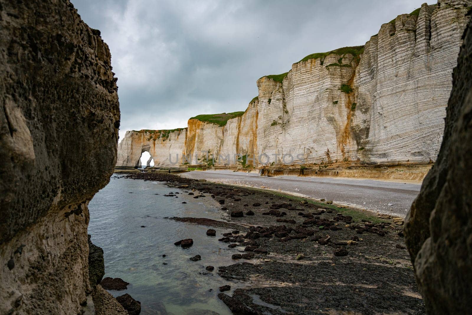 Landscape photo of tall, steep limestone cliffs by the ocean with one with a hole in it creating an arch view from the beach