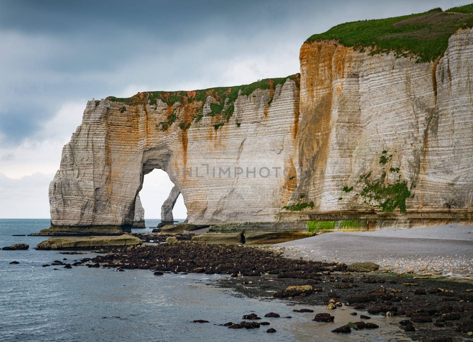 Landscape photo of tall, steep limestone cliffs by the ocean with one with a hole in it creating an arch view from the beach