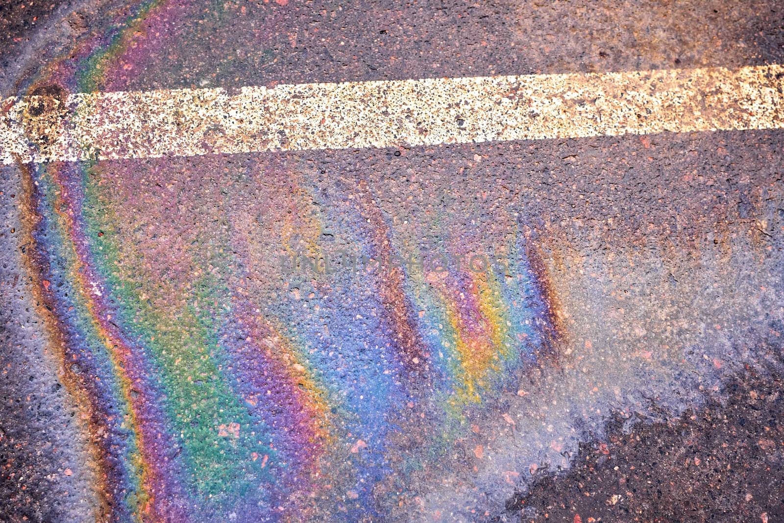 Oil spill on wet asphalt, parking lot with dividing lines. Highlighting environmental challenges related to water pollution