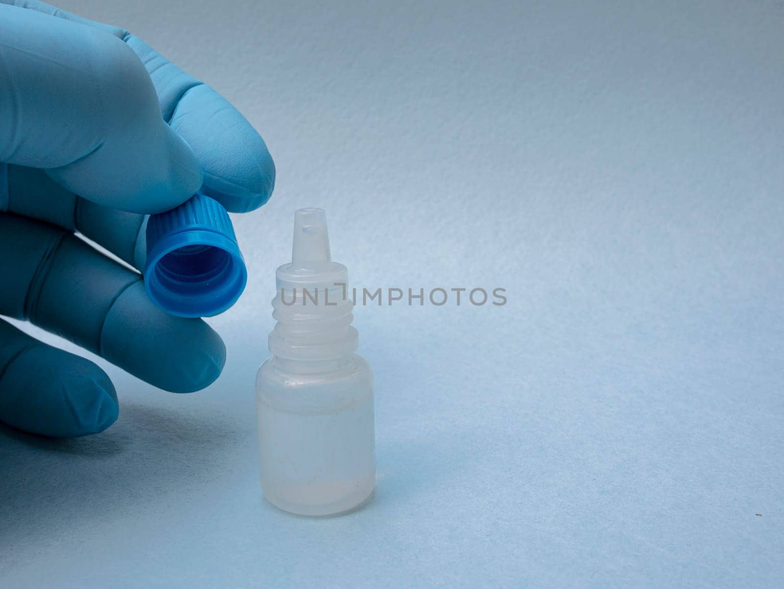 A man's hand in a blue glove close-up holds the cap of a plastic bottle with medicine close-up.