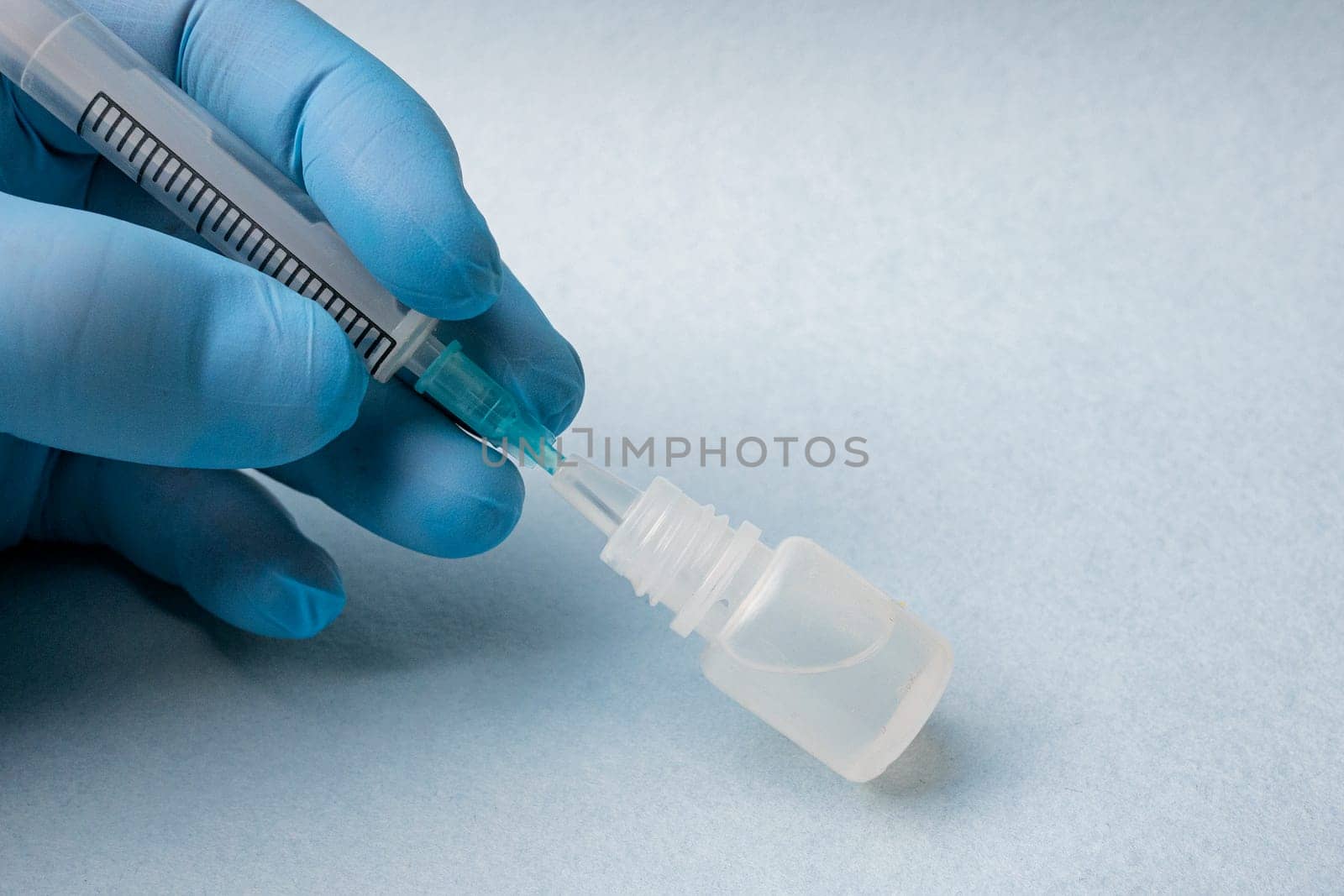 Close-up of a doctor's hand in a blue glove inserting a syringe into a bottle of medicine on a blue background.