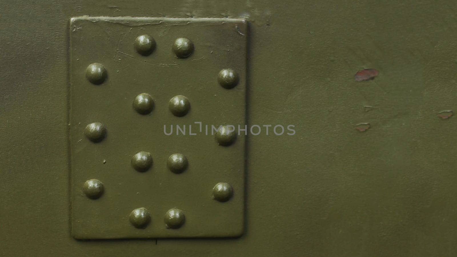Photo of a fragment of armor with rivets of a protective shield of military equipment.