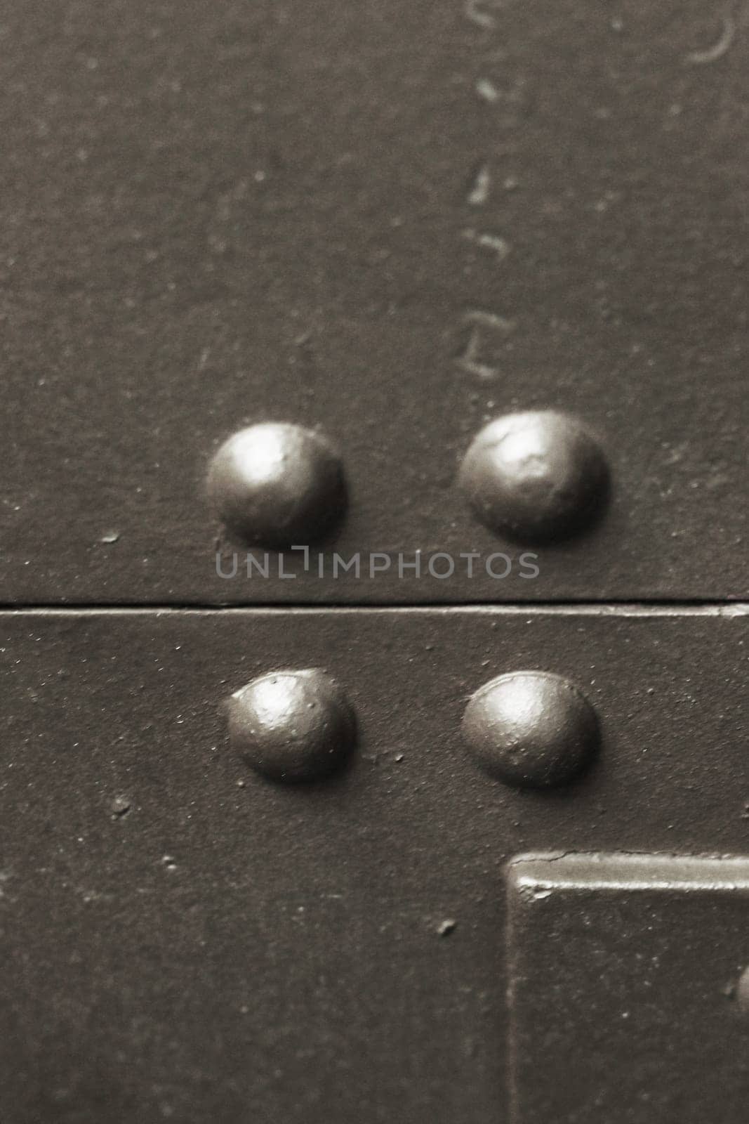 Close-up vertical photo of a fragment of armor with rivets of a protective shield from an artillery gun.
