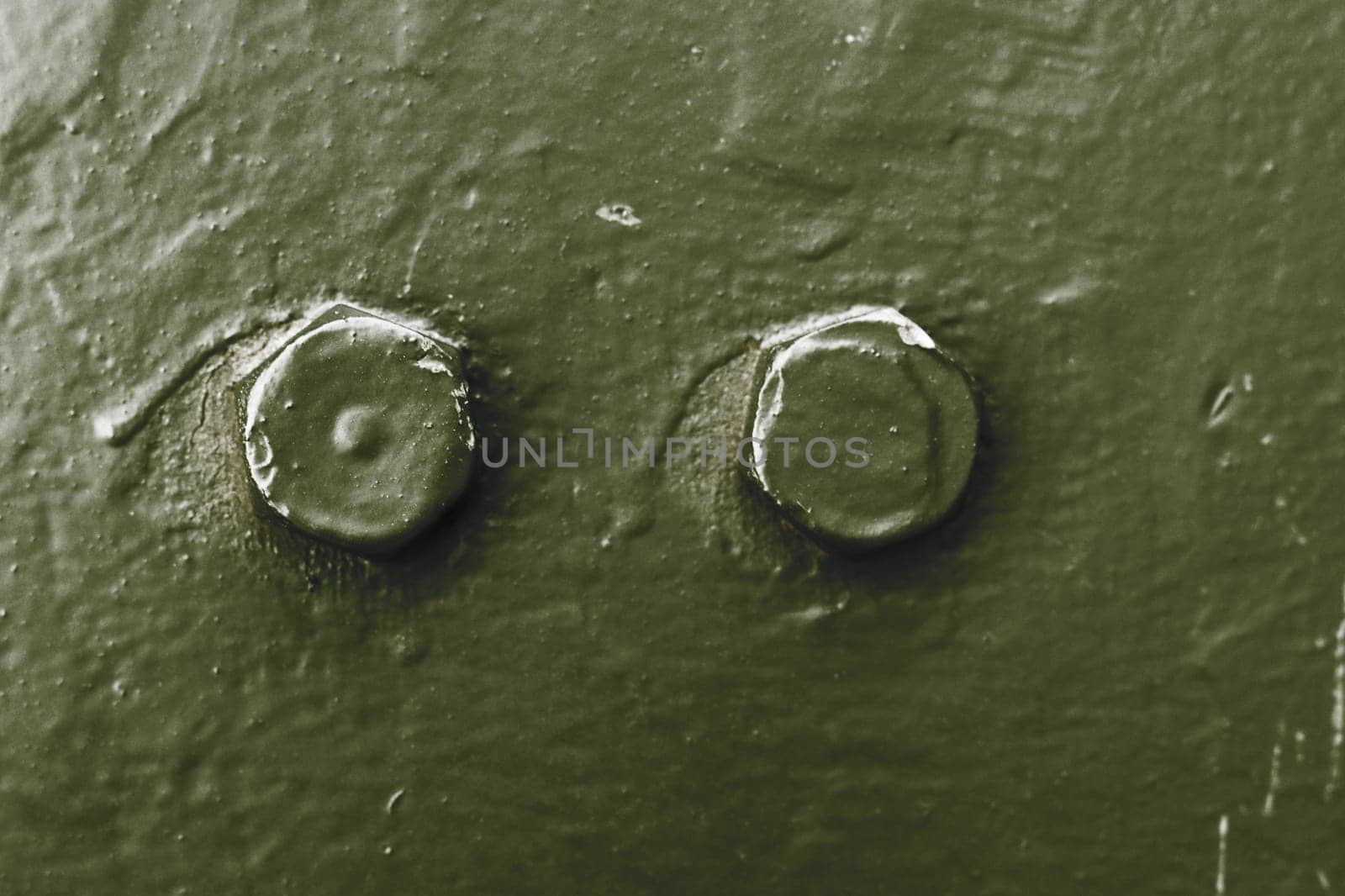 The metal surface of an armored vehicle with two bolts close-up, green.