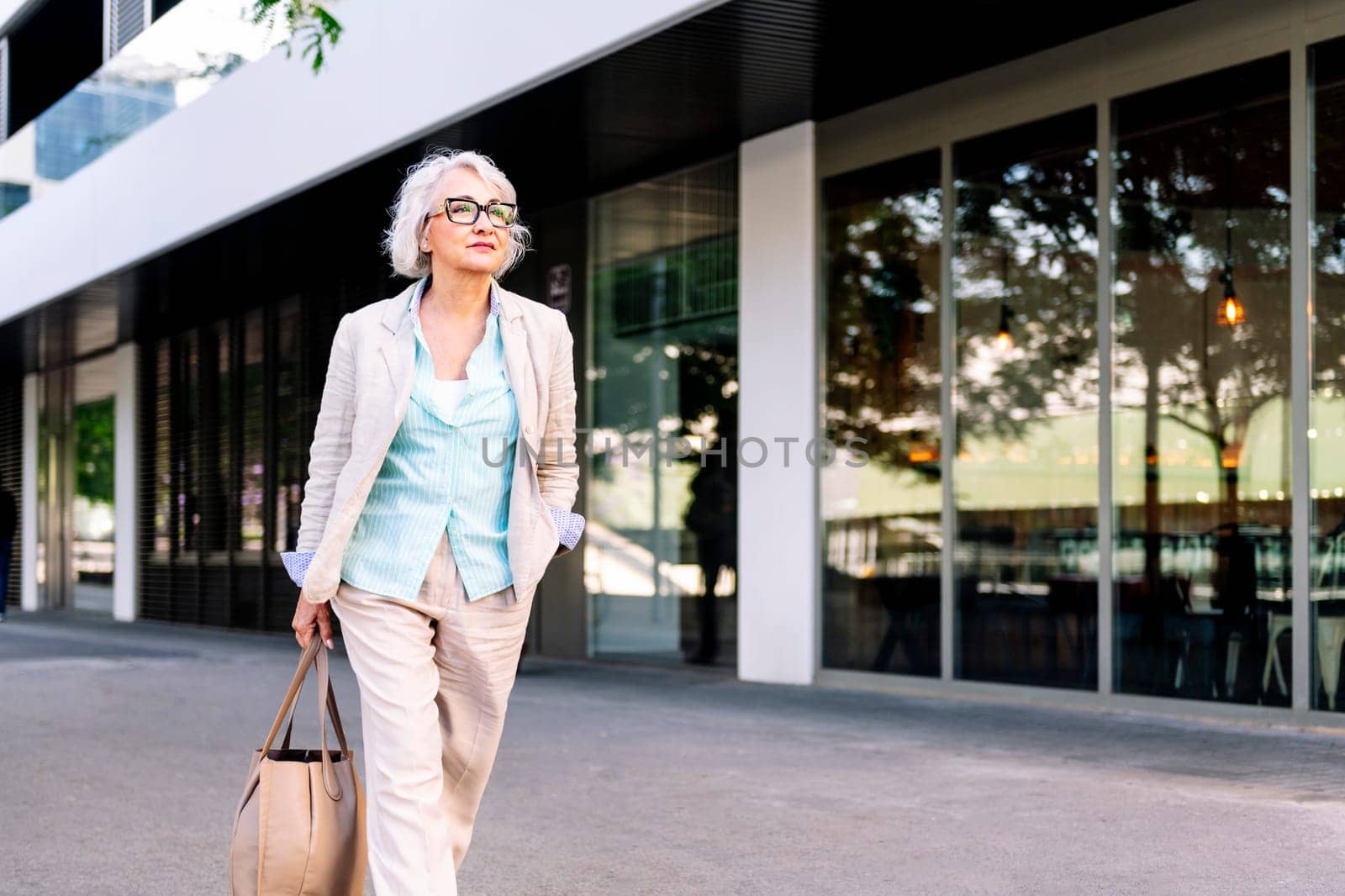 stylish mature woman walking with a bag in her hand next to a building, concept of urban lifestyle in adulthood, copyspace for text