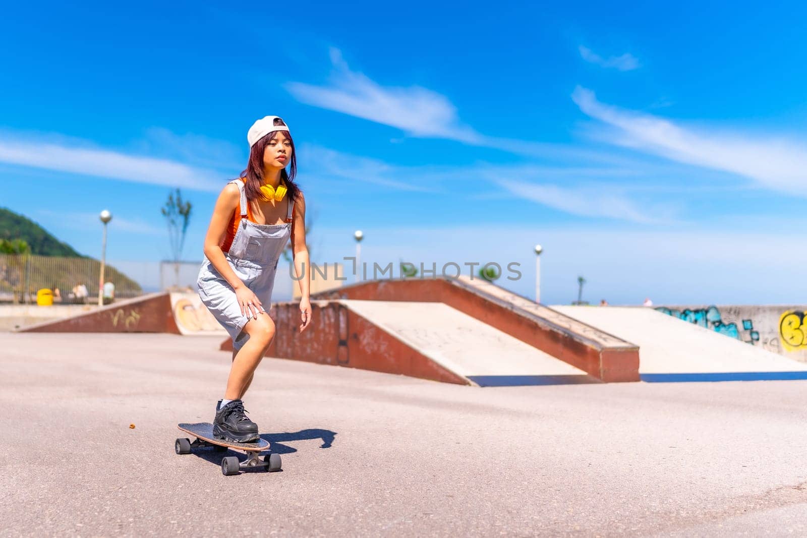 Full length photo of a young female cool asian skater practicing in an urban skateboard park
