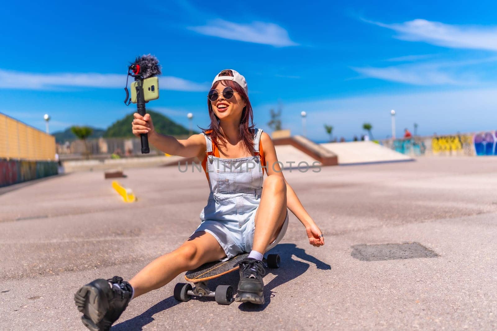 Smiling chinese female vlogger filming at skateboard park in summer