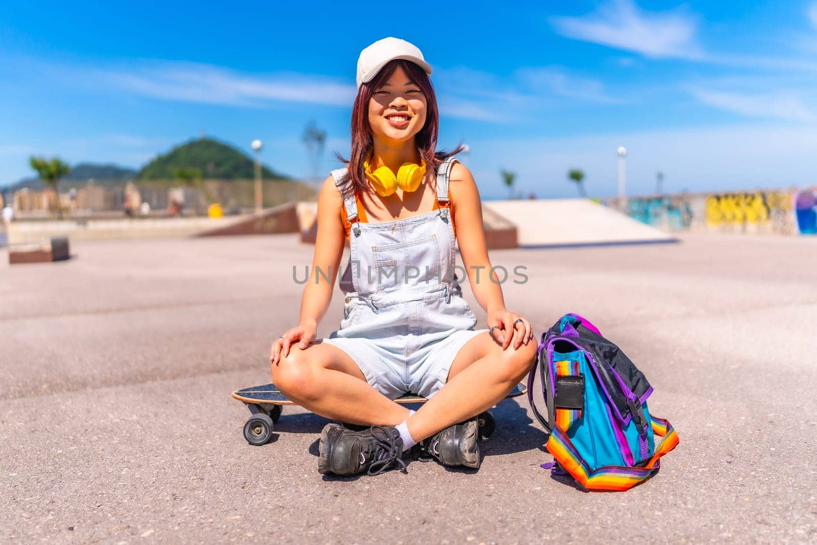 Asian woman sitting on skateboard smiling at camera in a public park
