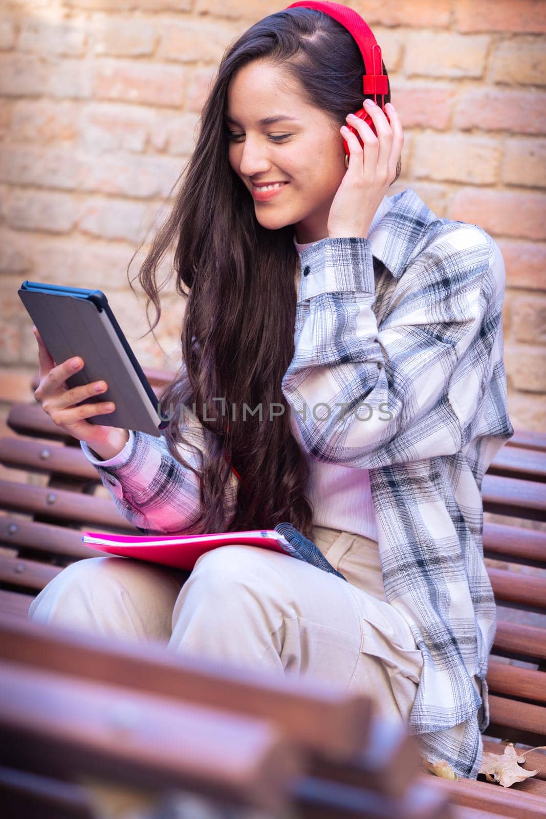 Young smiling student with notebook in hand uses social networks with tablet applications and wireless technology outdoors.Vertical