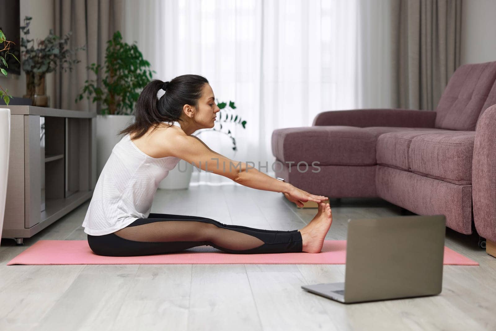 fit Caucasian woman worm up by stretching her body on pink exercise mat at home