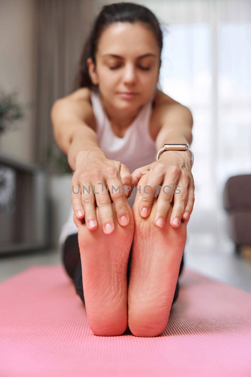 Sporty Caucasian woman worm up by stretching her body on pink exercise mat at home. focus on foot