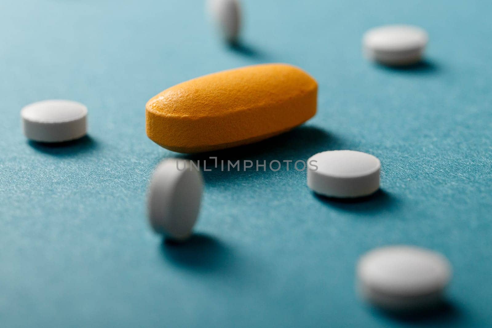 Close up of white and yellow pills on blue background.