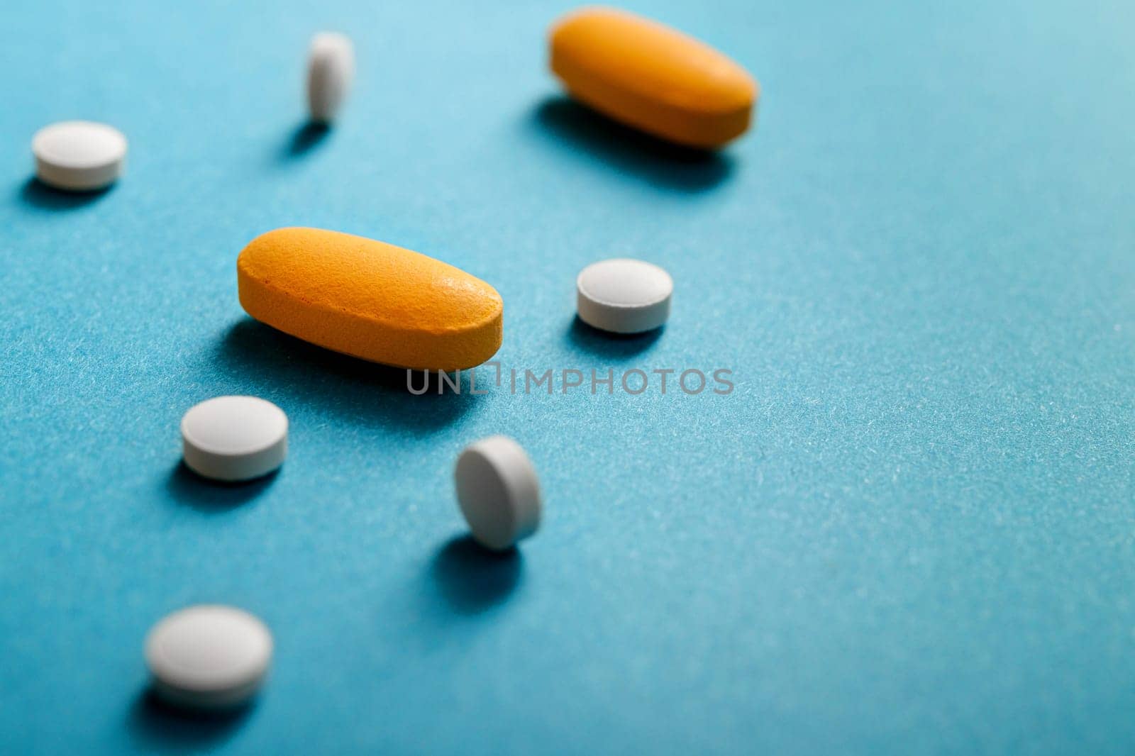White and yellow tablets and pills laid out on a blue background with copy space. Ideal for medical and healthcare topics.