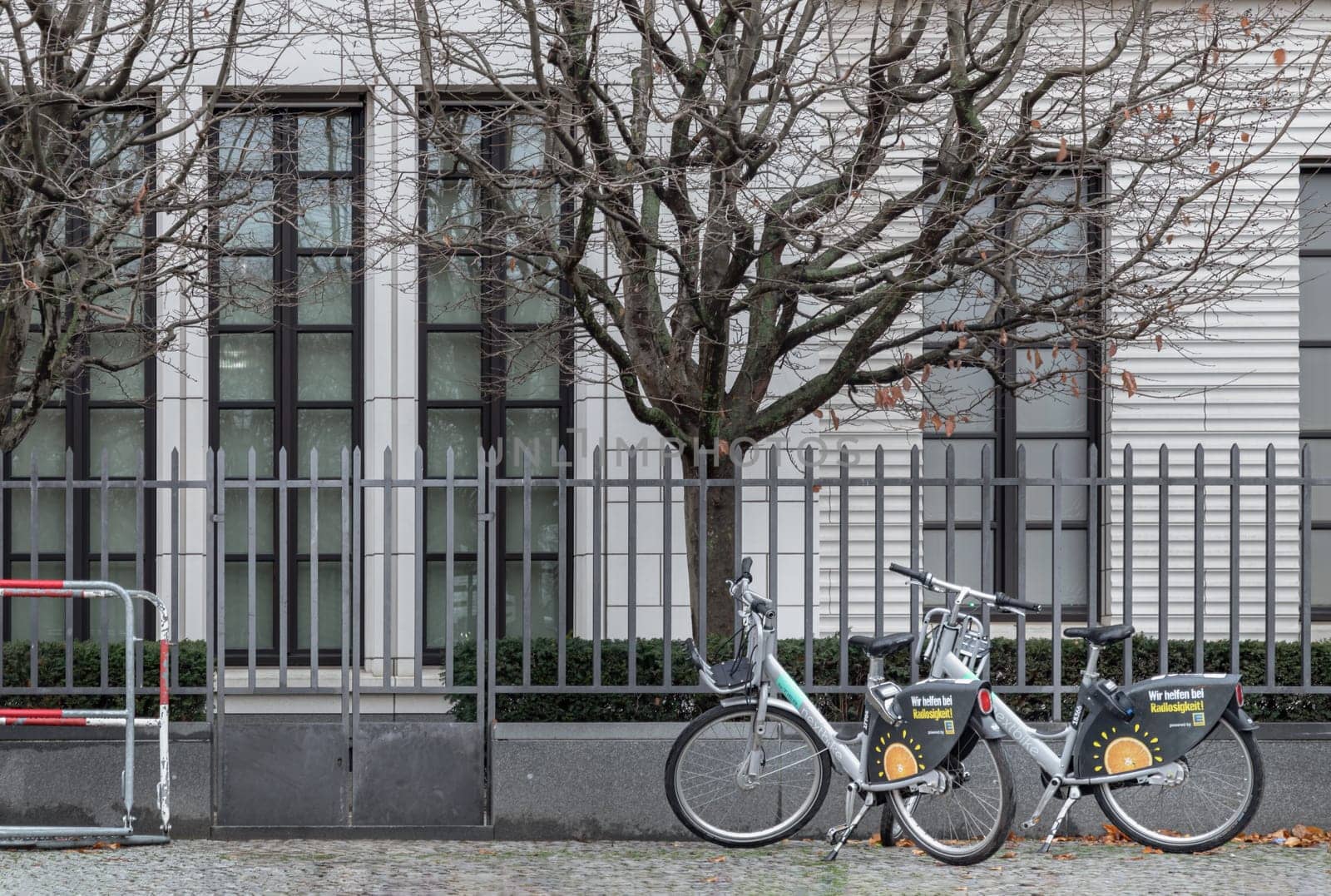 Berlin, Germany - Dec 20, 2023 - Two Bicycle parked at the side of iron fence the edge of road in downtown berlin. Space for text, Selective focus.