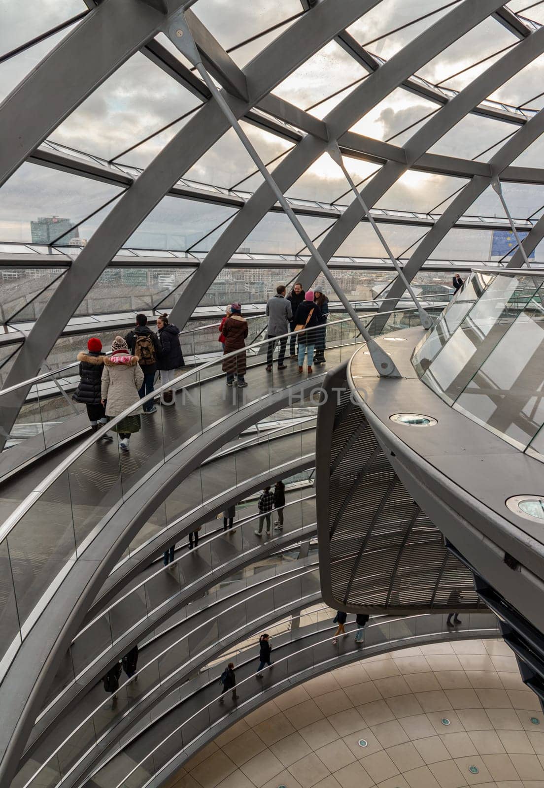Berlin, Germany - Dec 20, 2023 - Several tourists walking at ramps inside the futuristic glass dome. A curved walkway stretches in spirals upwards on top inside the Reichstag building. Contemporary architecture of the Cupola of the Reichstag dome, a major tourist attraction of the berlin city, Copy space, Selective focus.