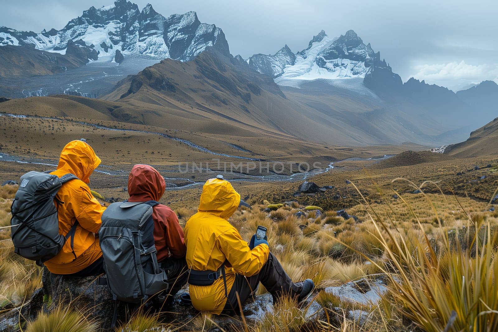 Three hikers wearing bright yellow and red raincoats sit on a mountain trail, taking a break. They have backpacks on and are looking out at the snowy peaks in the distance. The trail winds through a valley, and the ground is covered in dry grass. The sky is cloudy and the weather seems to be turning stormy.