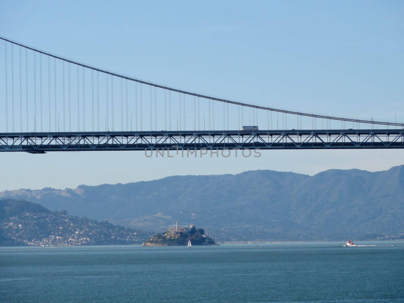 A panoramic view of the Bay Bridge with Alcatraz Island in the distance, featuring a small sailboat in the bay.